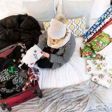 Jessica packing a suitcase on a bed with wrapped gifts around her
